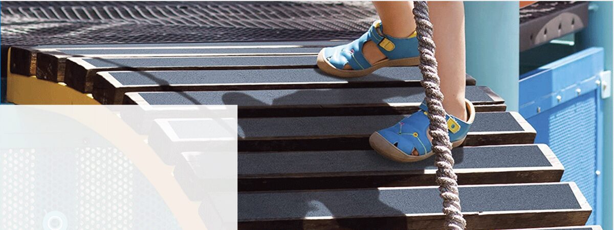 Child in sandals climbing outdoor playground steps covered with black anti-slip tape